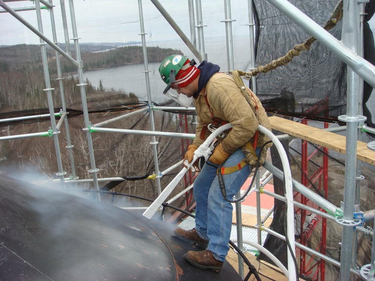 Specjalista pracujący z maszyną do czyszczenia suchym lodem ColdJet na wysokości przy renowacji kopuły zabytkowego gmachu. Operator w pełnej odzieży ochronnej i uprzęży bezpieczeństwa używa strumienia suchego lodu do precyzyjnego czyszczenia powierzchni kopuły.