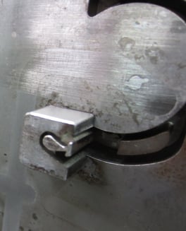 Zdjęcie przedstawia zbliżenie mechanicznego elementu z metalową powierzchnią, w której znajduje się zakrzywione wyżłobienie oraz mały, prostokątny zaczep osadzony w rowku. Widoczne są ślady zużycia i przebarwienia, co sugeruje intensywną eksploatację.